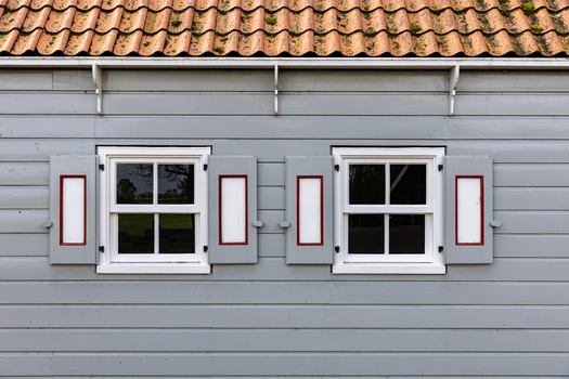 View of the traditional wooden facade of a historic building featuring grey siding and white framed windows with decorative shutters in Schokland Flevoland Netherlands.