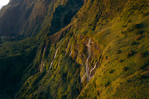 Aerial view of the Poco da Ribeira do Ferreiro waterfalls cascading down lush green cliffs during golden hour in Fajazinha Azores Portugal. Aerial view of the Poco da Ribeira do Ferreiro waterfalls cascading down lush green cliffs during golden hour in Fajazinha Azores Portugal.