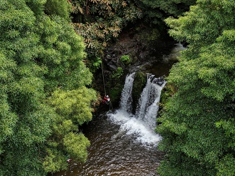 Aerial view of a person canyoning down a waterfall in Parque Natural da Ribeira dos Caldeiroes surrounded by lush green vegetation in Achada Acores Portugal. Aerial view of a person canyoning down a waterfall in Parque Natural da Ribeira dos Caldeiroes surrounded by lush green vegetation in Achada Acores Portugal.