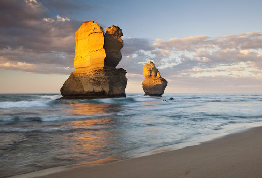 View of the Twelve Apostles limestone stacks standing in the ocean with waves crashing on the sandy beach under a golden sunset sky Australia. View of the Twelve Apostles limestone stacks standing in the ocean with waves crashing on the sandy beach under a golden sunset sky Australia.