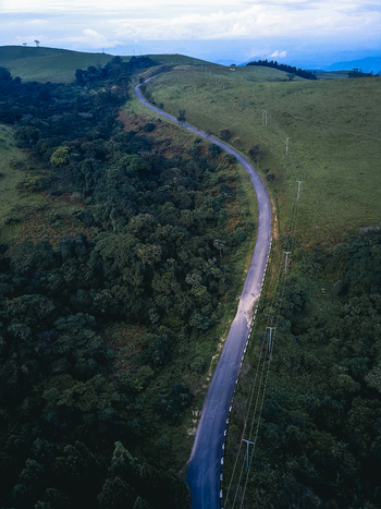 Aerial view of a winding road cutting through vibrant green hills and dark forest under a soft cloudy sky Obudu Cross River Nigeria.