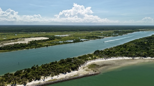 Aerial view of Matanzas Inlet featuring a scenic waterway with a boat wake sandy beaches and lush coastal vegetation in St. Johns County Florida United States. Aerial view of Matanzas Inlet featuring a scenic waterway with a boat wake sandy beaches and lush coastal vegetation in St. Johns County Florida United States.