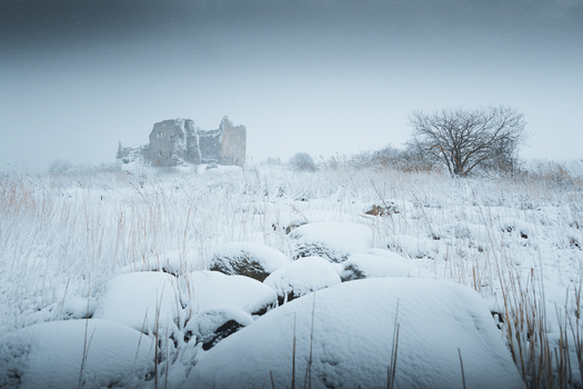 View of the snow covered ruins of Toolse fortress surrounded by a winter landscape with rocks and a bare tree in Toolse Laane Viru County Estonia. View of the snow covered ruins of Toolse fortress surrounded by a winter landscape with rocks and a bare tree in Toolse Laane Viru County Estonia.