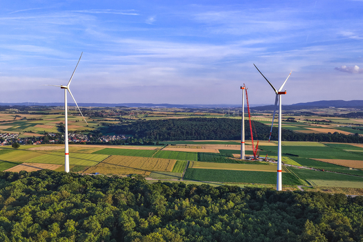 Aerial view of wind turbines in a rural landscape with one turbine under construction by a crane surrounded by agricultural fields and forest in Hofgeismar Hessen Germany.