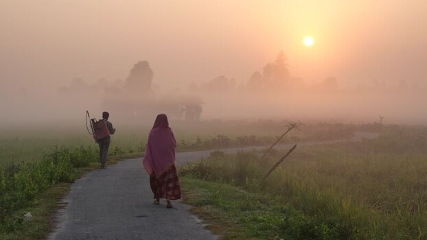 View of people walking on a foggy rural path at sunrise Bangladesh.