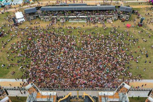 Herzogenaurach Germany 24 July 2025 Aerial view of the Open Beatz Festival with a large crowd gathered in front of the main stage and bar structures on a grassy field.