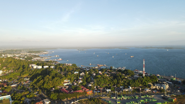Aerial view of the coastal city of Sorong featuring the harbor industrial port area lush green hills and ships anchored in the bay under a clear sky in Sorong Southwest Papua Indonesia. Aerial view of the coastal city of Sorong featuring the harbor industrial port area lush green hills and ships anchored in the bay under a clear sky in Sorong Southwest Papua Indonesia.