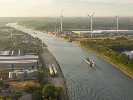 Aerial view of the Albertkanaal with industrial warehouses storage tanks wind turbines and a barge navigating the inland waterway in Genk Vlaanderen Belgium.