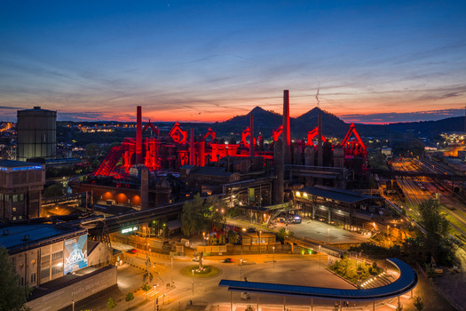 Volklingen Germany 09 May 2026 Aerial view of Volklingen Ironworks illuminated with red lights at dusk featuring smokestacks and industrial structures against a sunset sky. Volklingen Germany 09 May 2026 Aerial view of Volklingen Ironworks illuminated with red lights at dusk featuring smokestacks and industrial structures against a sunset sky.