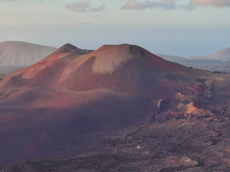 Aerial view of the volcanic landscape featuring red and dark volcanic soil craters and rugged terrain under soft light in Lanzarote. Aerial view of the volcanic landscape featuring red and dark volcanic soil craters and rugged terrain under soft light in Lanzarote.