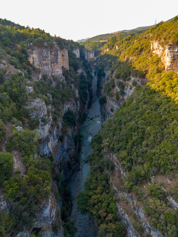Aerial view of Osumi canyon with steep limestone cliffs lush green vegetation and a river flowing through the gorge during golden hour in Dhores Berat County Albania.