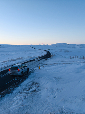 Aerial view of a car driving along a snow covered road through the winter landscape of Kirkjubaejarklaustur Skaftarhreppur Iceland. Aerial view of a car driving along a snow covered road through the winter landscape of Kirkjubaejarklaustur Skaftarhreppur Iceland.