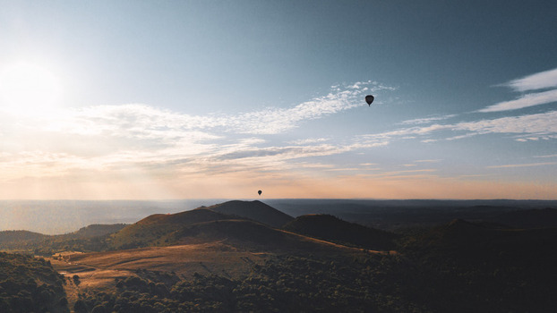 Aerial view of Puy de Dome with hot air balloons floating over the volcanic landscape during sunset in Orcines Auvergne Rhone Alpes France.