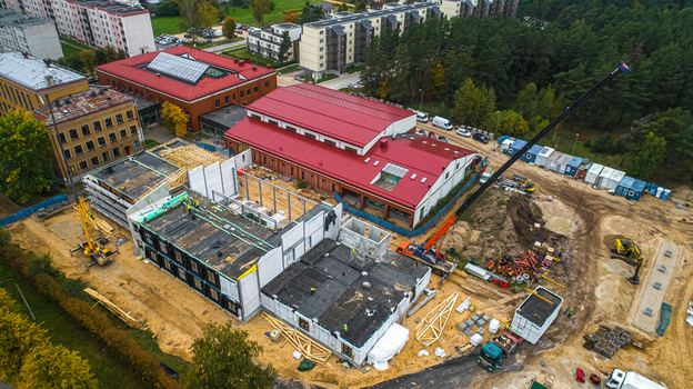 Aerial view of a construction site featuring a crane building framework and red roofed structures surrounded by trees in Latvia. Aerial view of a construction site featuring a crane building framework and red roofed structures surrounded by trees in Latvia.