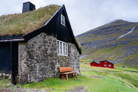 View of a traditional stone house with a grass roof and a wooden bench in the Faroe Islands.