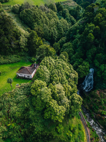 Aerial view of a quaint house nestled amidst a vibrant green forest with a cascading waterfall nearby Achada Açores Portugal. Aerial view of a quaint house nestled amidst a vibrant green forest with a cascading waterfall nearby Achada Açores Portugal.