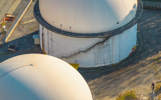 Aerial view of large white biogas storage domes with external metal stairways at an industrial anaerobic digestion facility in Italy. Aerial view of large white biogas storage domes with external metal stairways at an industrial anaerobic digestion facility in Italy.