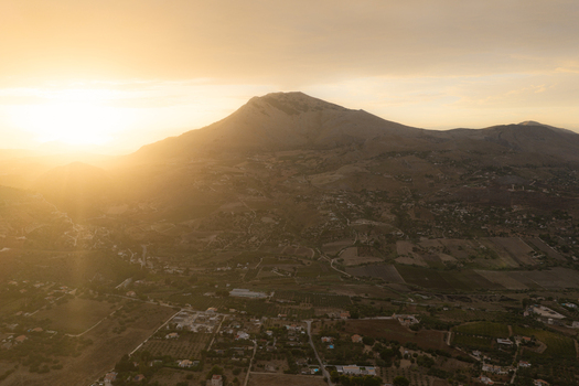 Aerial view of Riserva Naturale Orientata dello Zingaro at sunset with golden light illuminating the mountain slopes rural fields and scattered buildings in San Vito Lo Capo Sicilia Italy. Aerial view of Riserva Naturale Orientata dello Zingaro at sunset with golden light illuminating the mountain slopes rural fields and scattered buildings in San Vito Lo Capo Sicilia Italy.