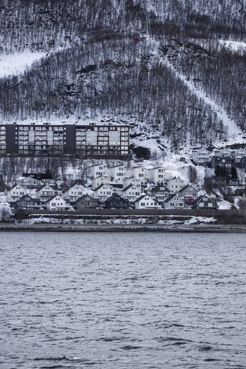 View of modern residential buildings and houses on a snowy hillside by the water in Tromso Troms Norway.