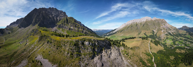Aerial view of the majestic mountains draped in green and grey hues under a blue sky pathways winding through the landscape La Clusaz Auvergne Rhône Alpes France. Aerial view of the majestic mountains draped in green and grey hues under a blue sky pathways winding through the landscape La Clusaz Auvergne Rhône Alpes France.