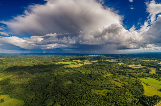 Aerial view of the vast green forests and agricultural fields under a dramatic storm cloud formation in Latvia. Aerial view of the vast green forests and agricultural fields under a dramatic storm cloud formation in Latvia.
