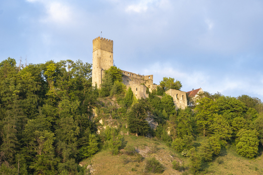 View of Randeck Castle ruins perched on a lush green hill with a tall stone tower under a soft blue sky in Essing Bayern Germany.