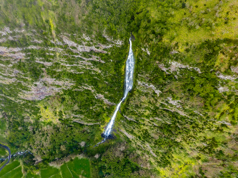 Aerial view of a cascade plunges down the verdant cliffside a ribbon of white against the rugged moss covered stone Faj&atilde; Grande Azores Portugal.