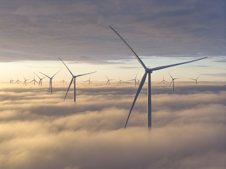 Aerial view of a modern wind farm with turbines emerging from a thick layer of white clouds under a soft golden sunrise sky Netherlands. Aerial view of a modern wind farm with turbines emerging from a thick layer of white clouds under a soft golden sunrise sky Netherlands.