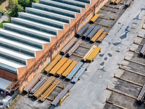 Aerial view of an industrial warehouse with a sawtooth roof and stacks of metal pipes in an outdoor storage yard Dalmine Lombardy Italy. Aerial view of an industrial warehouse with a sawtooth roof and stacks of metal pipes in an outdoor storage yard Dalmine Lombardy Italy.