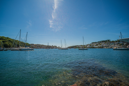View of sailboats moored in the Fowey River with the historic town of Fowey in the background under a clear blue sky in Fowey Cornwall United Kingdom. View of sailboats moored in the Fowey River with the historic town of Fowey in the background under a clear blue sky in Fowey Cornwall United Kingdom.