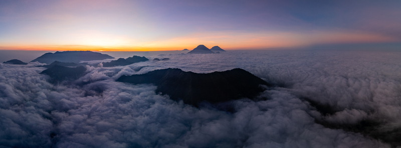 Aerial view of Gunung Bismo rising above a dense sea of clouds during a vibrant sunrise in Kecamatan Kejajar Jawa Tengah Indonesia.