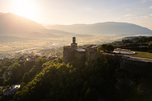 Aerial view of the Castle of Gjirokastra with its clock tower and stone walls overlooking a misty valley and mountains at sunset in Gjirokaster Qarku i Gjirokastres Albania. Aerial view of the Castle of Gjirokastra with its clock tower and stone walls overlooking a misty valley and mountains at sunset in Gjirokaster Qarku i Gjirokastres Albania.