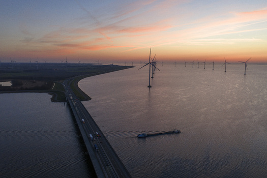 Aerial view of Ketelbrug bridge with traffic offshore wind turbines in the water and a barge under a sunset sky Nagele Flevoland Netherlands.