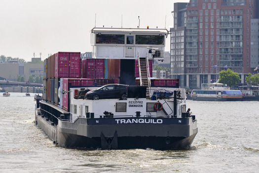 Dordrecht Netherlands 31 May 2026 View of the inland container ship Tranquilo navigating the Oude Maas river carrying colorful shipping containers and a car on deck past the urban waterfront.