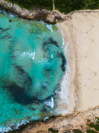 Aerial view of Cala Mendia beach featuring turquoise waters white sand and rocky cliffs with a stone staircase in Cala Mendia Illes Balears Spain. Aerial view of Cala Mendia beach featuring turquoise waters white sand and rocky cliffs with a stone staircase in Cala Mendia Illes Balears Spain.