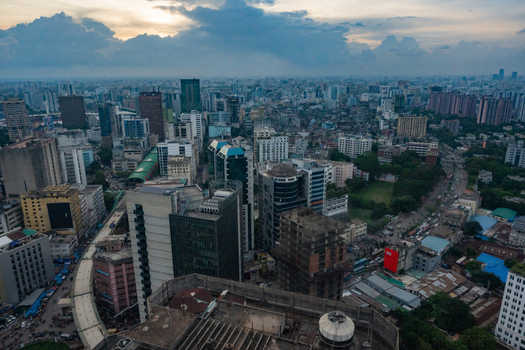 Dhaka Bangladesh 30 June 2025 Aerial view of the dense urban skyline of Dhaka featuring modern high rise buildings busy streets and lush green spaces under a cloudy sunset sky.