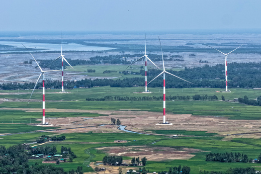 Aerial view of wind turbines with red and white stripes rising from the green fields towards the hazy horizon Cox s Bazar Chittagong Division Bangladesh. Aerial view of wind turbines with red and white stripes rising from the green fields towards the hazy horizon Cox s Bazar Chittagong Division Bangladesh.