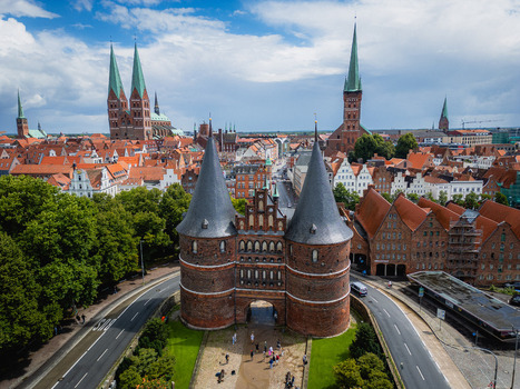 Aerial view of the iconic Holstentor gate stands guard its dark towers contrasting against the vibrant red rooftops and the distant spires of St. Mary s Church L&uuml;beck Schleswig Holstein Germany.