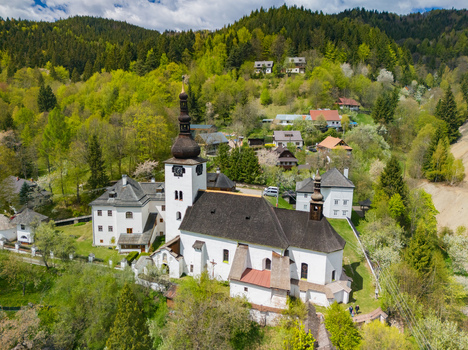 Aerial view of the Church of the Conversion of the Lord and historic houses nestled in lush green hills in Spania Dolina Banska Bystrica Region Slovakia.