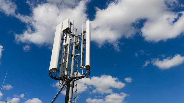 Aerial view of a telecommunications tower with white panel antennas against a bright blue sky with scattered white clouds in Amsterdam North Holland Netherlands. Aerial view of a telecommunications tower with white panel antennas against a bright blue sky with scattered white clouds in Amsterdam North Holland Netherlands.