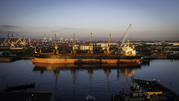 Aerial view of a large cargo ship docked at a busy industrial port with towering cranes and containers in the background in New York New York United States. Aerial view of a large cargo ship docked at a busy industrial port with towering cranes and containers in the background in New York New York United States.