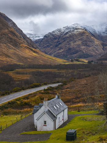 Aerial view of Lagangarbh Hut at the foot of snow capped mountains in Glencoe with a winding road and dramatic clouds Scotland United Kingdom. Aerial view of Lagangarbh Hut at the foot of snow capped mountains in Glencoe with a winding road and dramatic clouds Scotland United Kingdom.