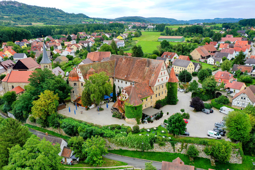 Aerial view of Schloss Wiesenthau featuring its historic architecture and red tiled roofs surrounded by the village and lush greenery in Wiesenthau Bayern Germany. Aerial view of Schloss Wiesenthau featuring its historic architecture and red tiled roofs surrounded by the village and lush greenery in Wiesenthau Bayern Germany.