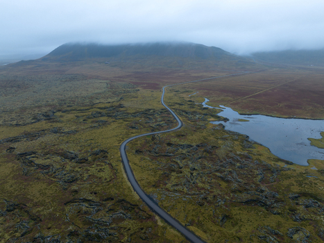 Aerial view of a winding road cutting through the mossy textured landscape leading towards a misty mountain Snæfellsnes Eyja og Miklaholtshreppur Iceland. Aerial view of a winding road cutting through the mossy textured landscape leading towards a misty mountain Snæfellsnes Eyja og Miklaholtshreppur Iceland.