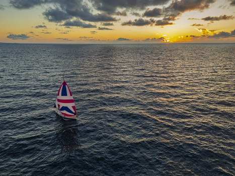 Aerial view of a sailboat with a colorful patterned sail gliding across the deep blue ocean during a golden sunset in Waimea Hawaii United States. Aerial view of a sailboat with a colorful patterned sail gliding across the deep blue ocean during a golden sunset in Waimea Hawaii United States.