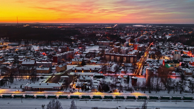 Aerial view of a snow covered town at sunset with a freight train on the tracks and residential buildings in Latvia. Aerial view of a snow covered town at sunset with a freight train on the tracks and residential buildings in Latvia.