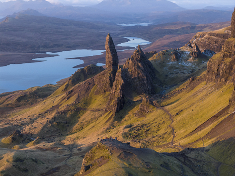 Aerial view of The Storr rock formation with people standing on a ridge and a lake in the background during golden hour in Isle of Skye Scotland United Kingdom. Aerial view of The Storr rock formation with people standing on a ridge and a lake in the background during golden hour in Isle of Skye Scotland United Kingdom.