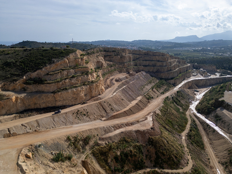Aerial view of a large open pit stone quarry with terraced rock faces dirt access roads and heavy machinery in Teulada Valencian Community Spain.