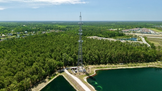 Aerial view of a tall telecommunications tower rising above a lush green forest next to a calm pond World Golf Village Florida United States. Aerial view of a tall telecommunications tower rising above a lush green forest next to a calm pond World Golf Village Florida United States.