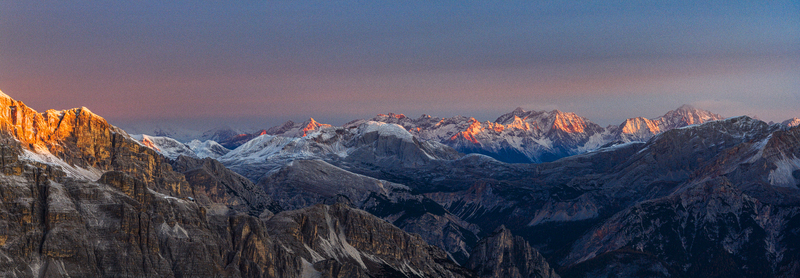 Aerial view of the rugged Alps mountains snow dusted peaks catch the warm glow of the rising sun contrasting sharply with the cool shadows nestled in the valleys Veneto Italy.